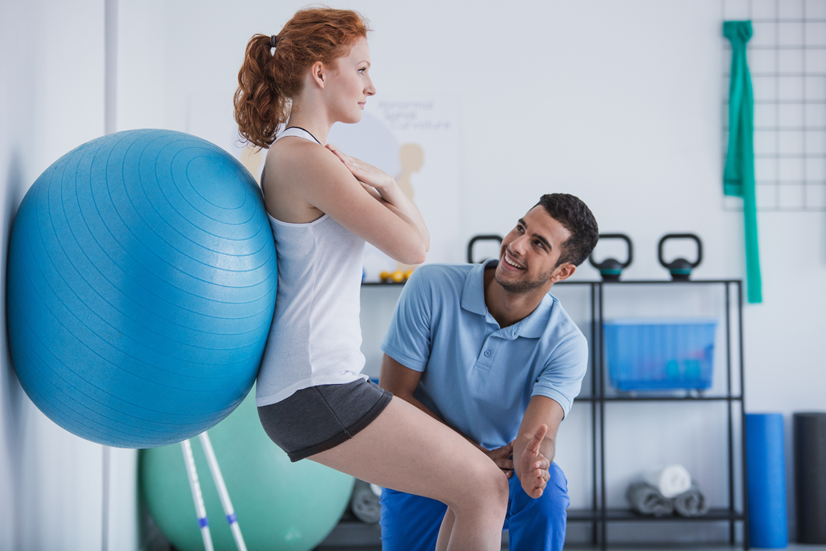 Smiling professional personal trainer helping sportswoman exerci